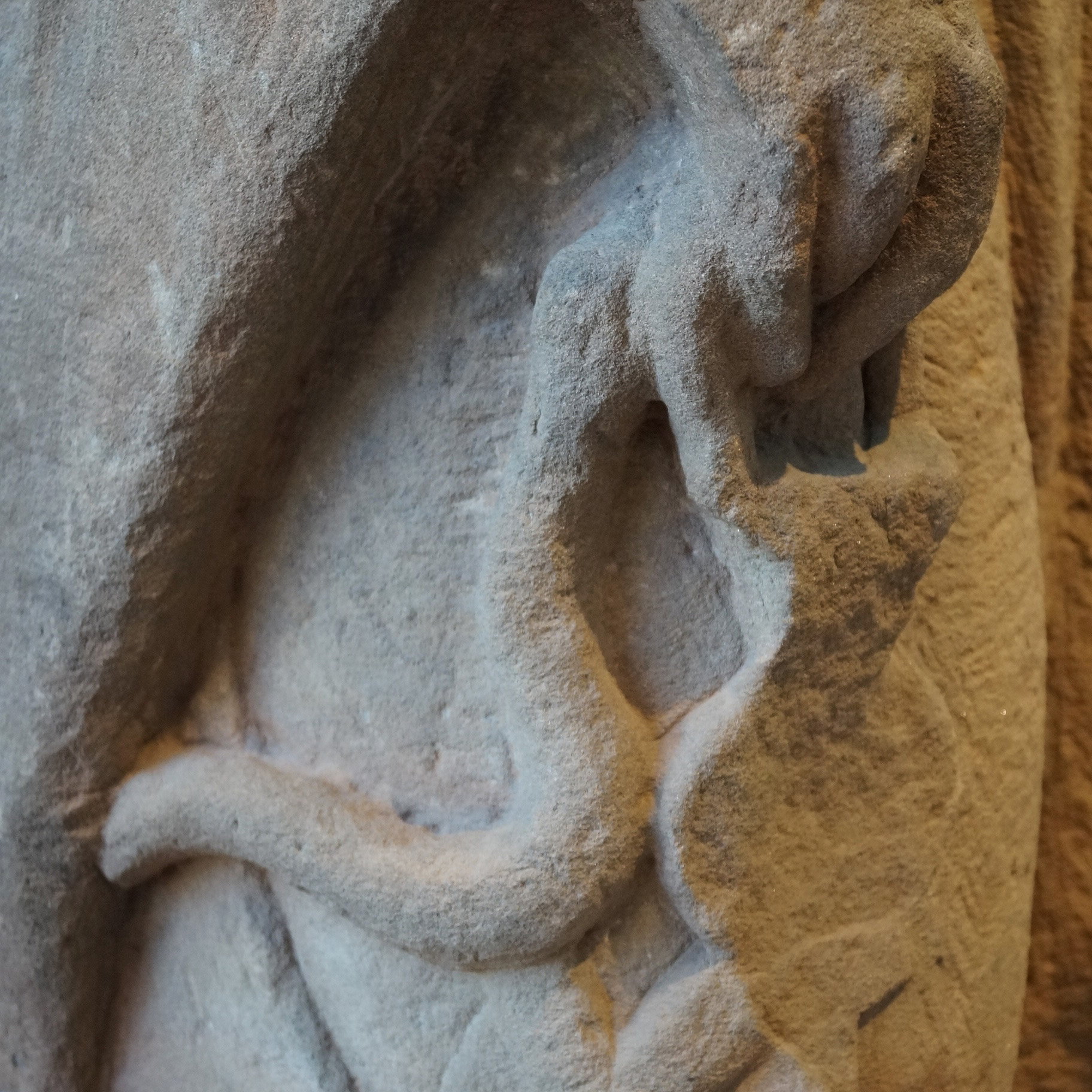 Detailfoto einer steinernen römischen Grabstatue mit dem Reliefdarstellung einer Hand, die eine Badegarnitur aus Strigilis, Ölfläschchen und Badesandalen hält. Rheinisches Landesmuseum Trier.