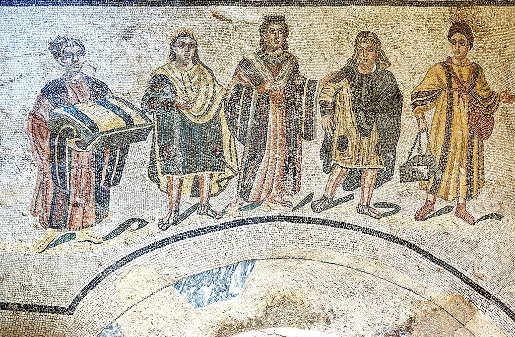 Ein römisches Mosaik zeigt eine reiche Römerin, die begleitet von ihren vier Dienerinnen, die das Badezubehör tragen, in die Thermen geht.